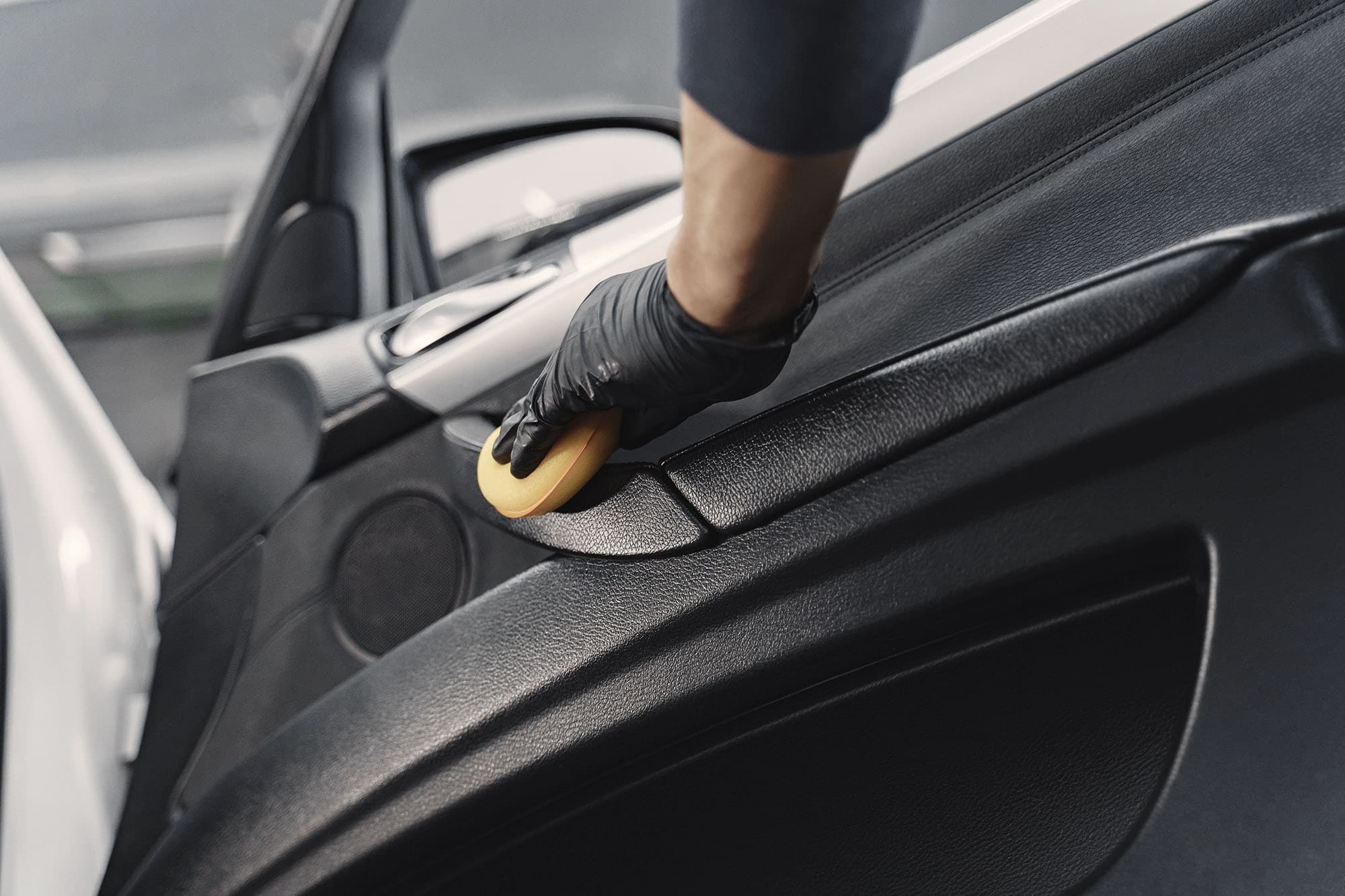 Na zdjęciu widać rękę w rękawiczce, która starannie czyści wnętrze drzwi samochodu za pomocą ściereczki. Mycie ręczne Dzierżoniów dostępne w Kasprowicz Auto.